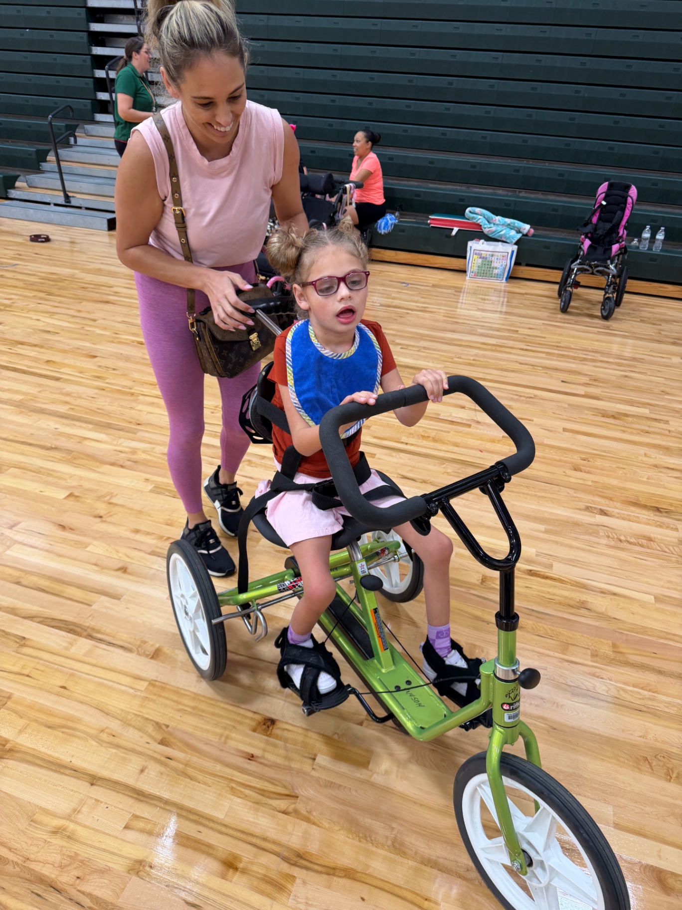Ava riding an adaptive bike with help during therapy